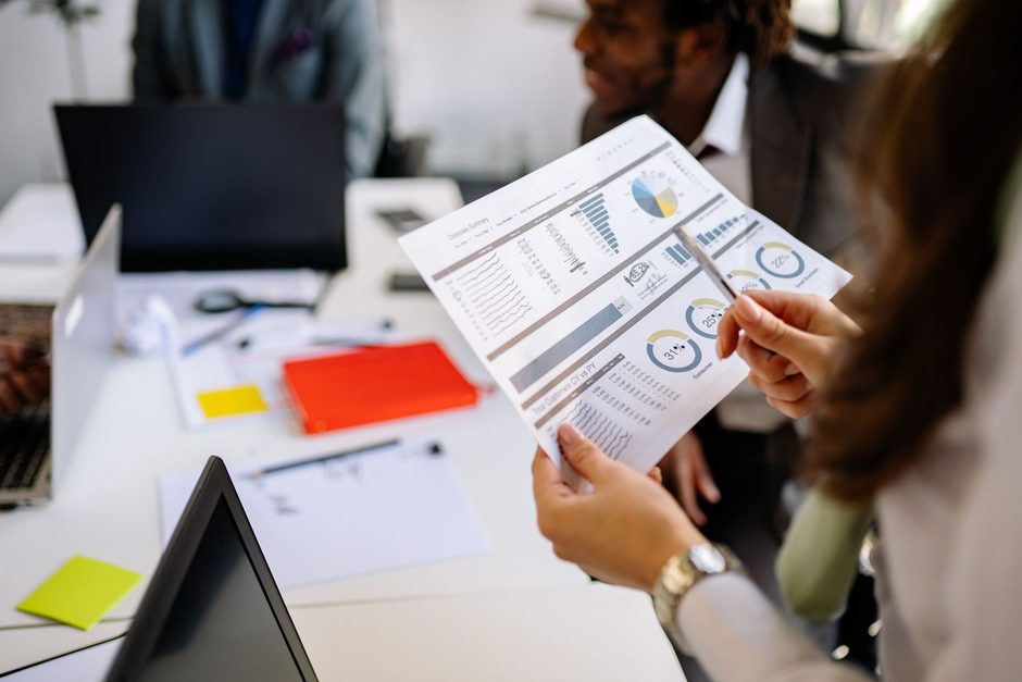 Marketer reviewing printed performance reports with a laptop open on the desk. Photo by Yan Krukau on Pexels