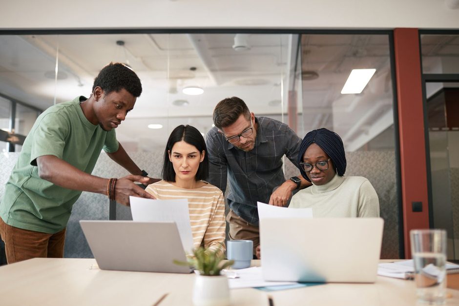 Marketing team gathered around laptops in a bright office reviewing creative work. Photo by Theo  Decker on Pexels