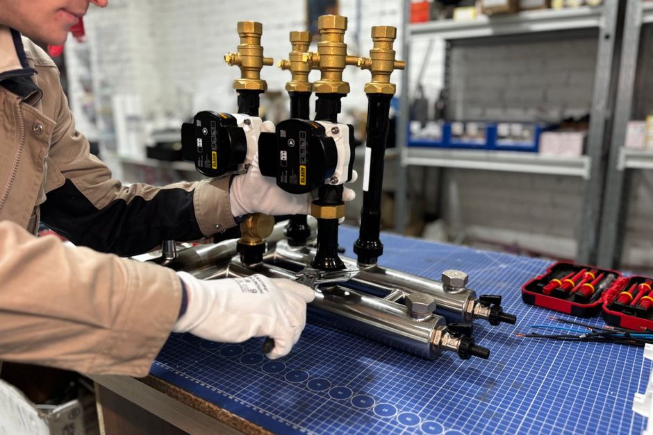 Technician working on brass HVAC manifold pipes and gauges at a workbench. Photo by МОБО Модульные Котельные on Pexels