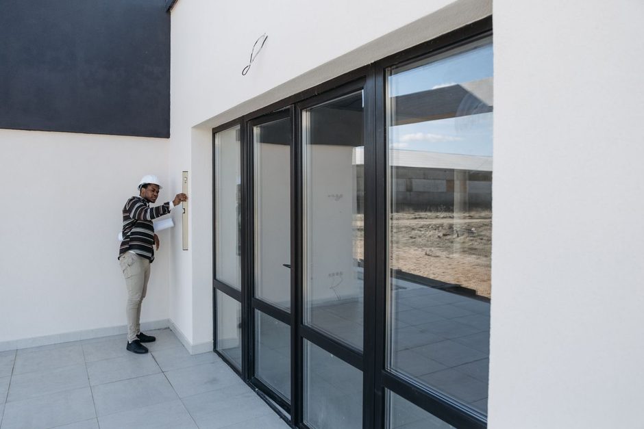 Installer standing beside large black framed glass doors and windows of a modern building. Photo by Pavel Danilyuk on Pexels