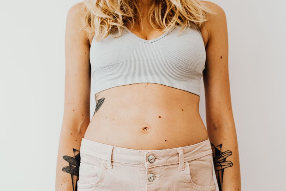 Close-up of a woman's midsection wearing a sports bra, showcasing tattoos and casual style. Photo by https://kaboompics.com/ on Pexels