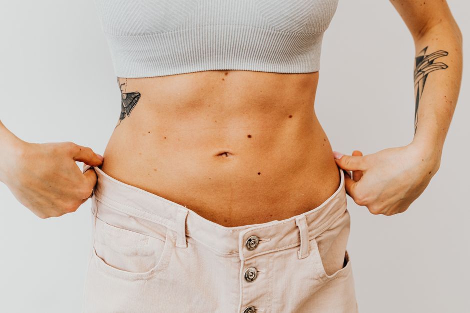 Photo by https://kaboompics.com/ on Pexels A woman shows weight loss progress by holding loose pants around her waist, highlighting tattoos. Photo by https://kaboompics.com/ on Pexels