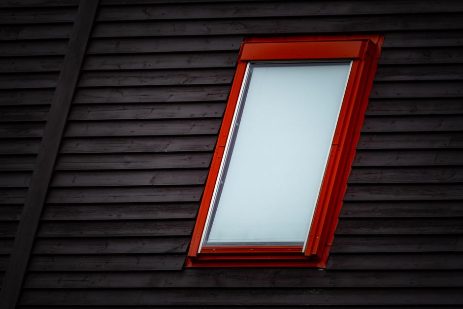 Close-up of a skylight with a red frame embedded in a dark wooden rooftop. Photo by Francesco Ungaro on Pexels