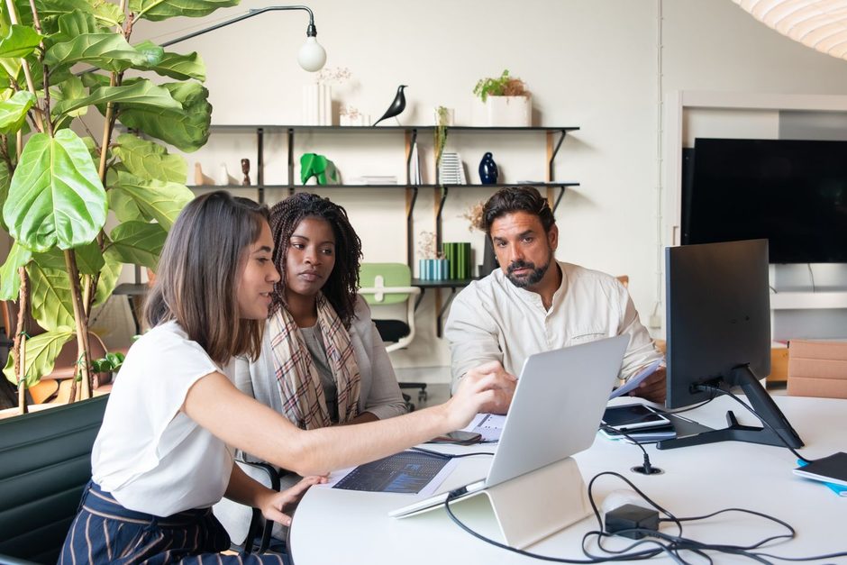 Colleagues gathered around laptops at a table in a bright modern office. Photo by Kampus Production on Pexels