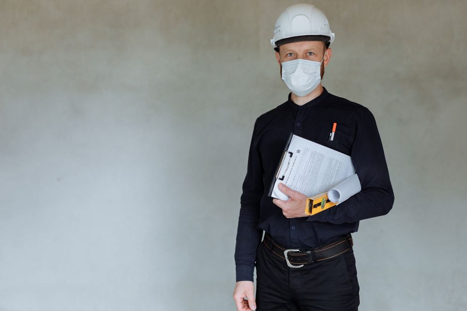 Inspector in a hard hat and face mask holding a clipboard. Photo by Thirdman on Pexels
