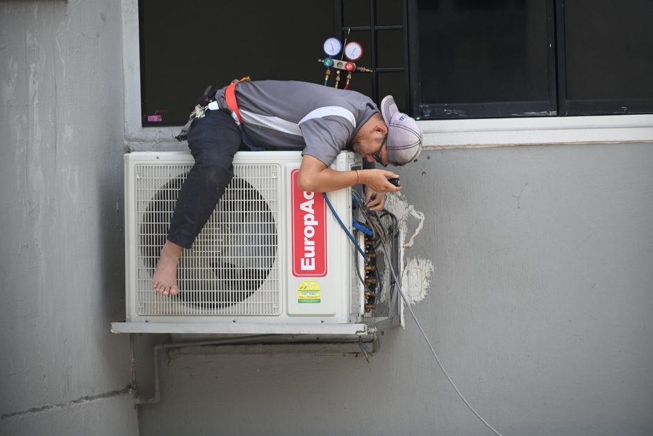 Technician installing an air conditioner unit on an exterior wall. Photo by Richard Low Hong on Pexels