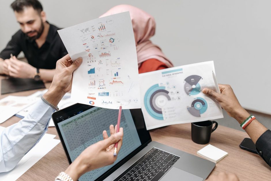 Team members reviewing printed charts and a laptop together at a table. Photo by Pavel Danilyuk on Pexels