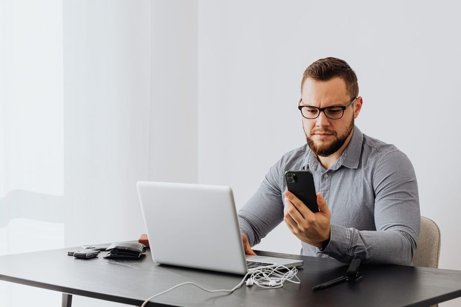 Photo by https://kaboompics.com/ on Pexels Business owner checking a phone beside an open laptop at a bright desk. Photo by https://kaboompics.com/ on Pexels