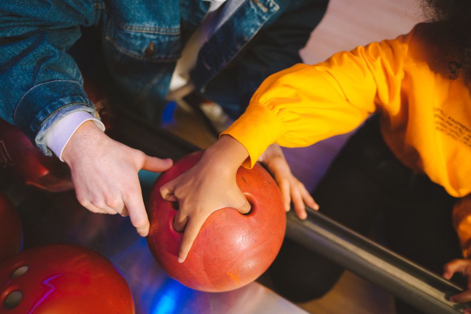 Close-up of hands preparing a red bowling ball in a vibrant bowling alley setting. Photo by Anastasia  Shuraeva on Pexels