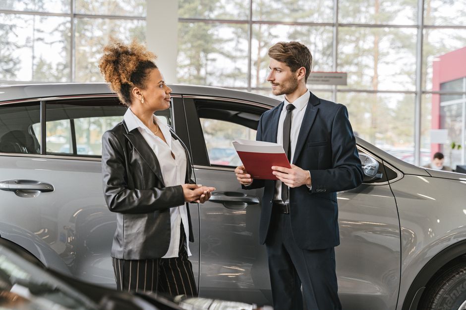 A woman discussing car purchase with a dealer inside a car dealership showroom. Photo by Antoni Shkraba on Pexels