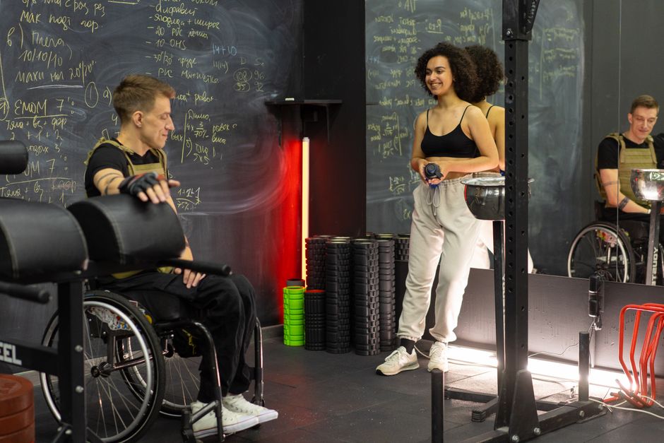 Photo by Mikhail Nilov on Pexels Two people in a gym, one in a wheelchair and one standing, preparing for a workout. Photo by Mikhail Nilov on Pexels