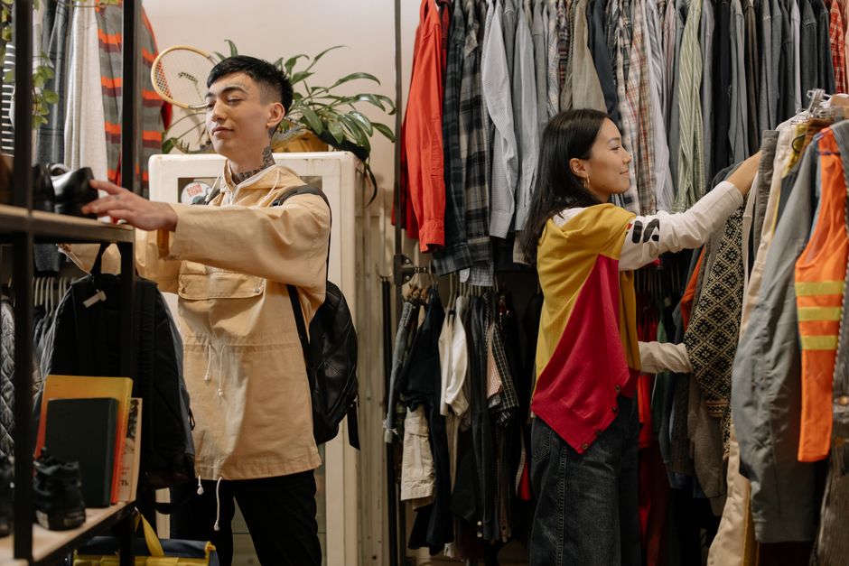 Two young adults selecting clothes in a crowded vintage thrift store. Photo by cottonbro studio on Pexels