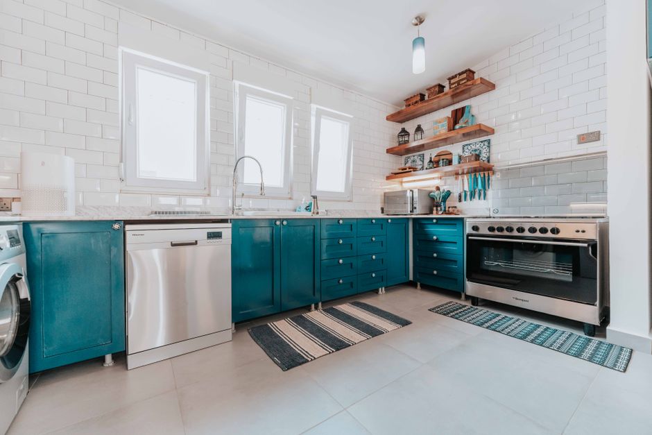 Bright modern kitchen with blue cabinets, stainless steel appliances, and open shelving. Photo by Keegan Checks on Pexels
