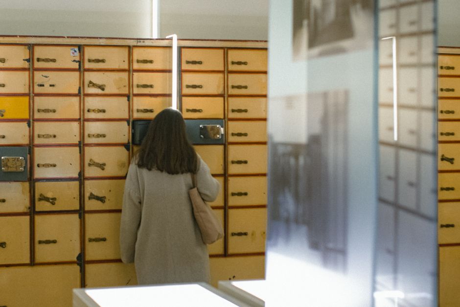 Woman with long brown hair looking at vintage mailboxes in an indoor setting. Photo by Berna on Pexels