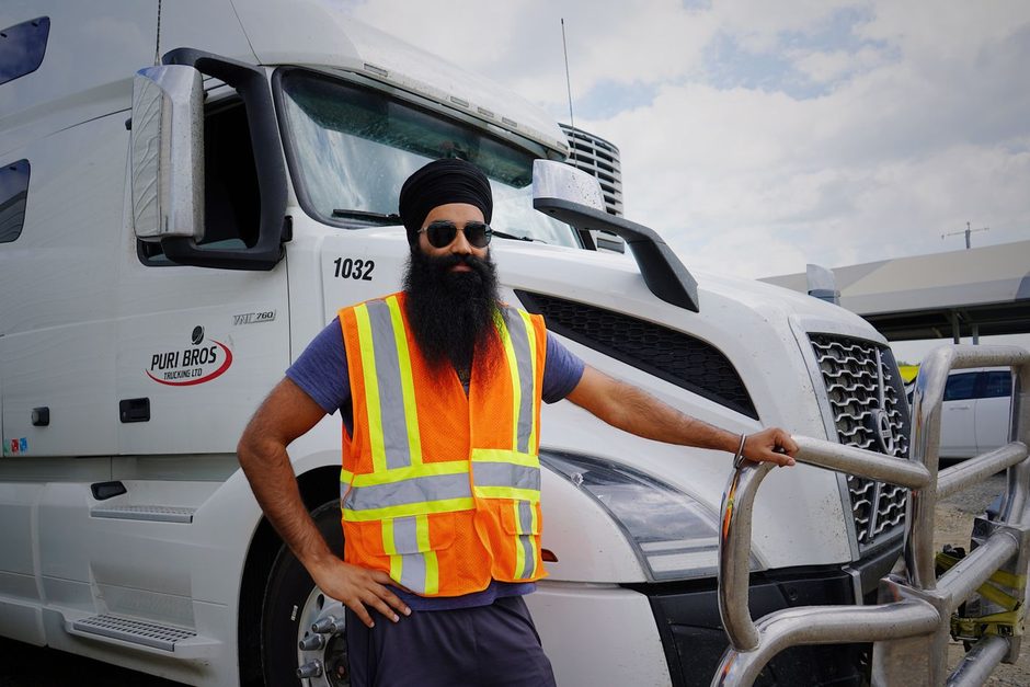 Truck driver in a hi-vis vest standing beside a white lorry. Photo by World Sikh Organization of Canada on Pexels