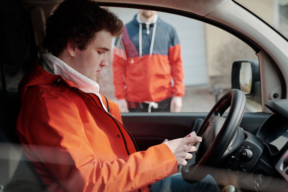 Photo by Norma Mortenson on Pexels Driver in an orange jacket checking a phone inside a car. Photo by Norma Mortenson on Pexels
