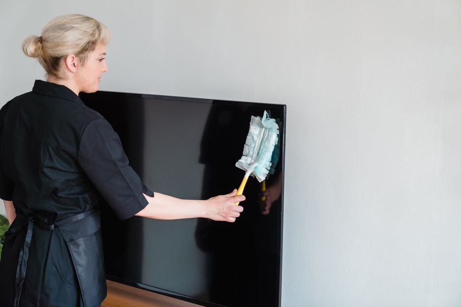 A female housekeeper performing dusting on a television screen indoors. Photo by Liliana Drew on Pexels
