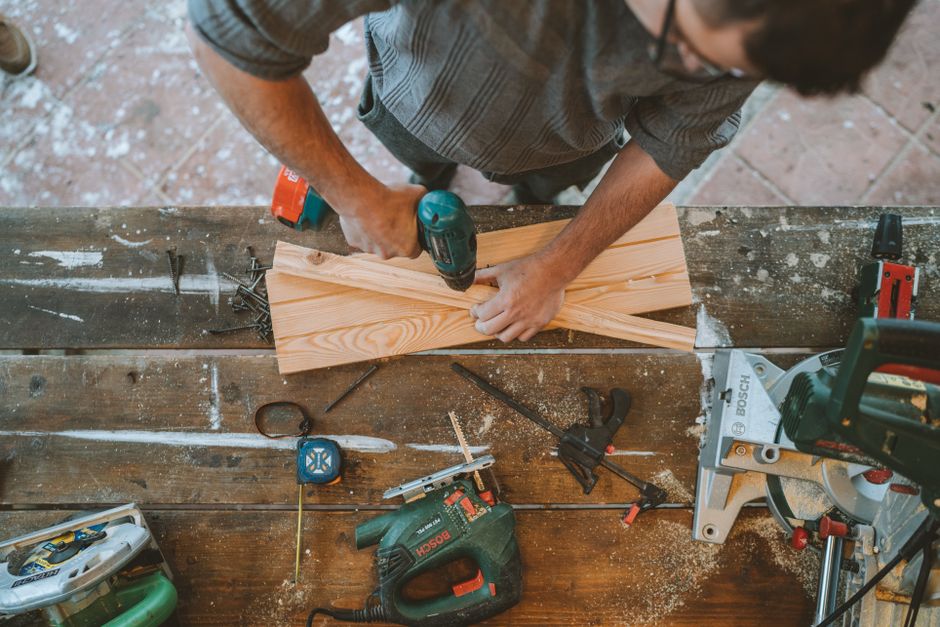 Craftsman busy drilling wooden planks in a carpentry workshop with various tools around. Photo by Anastasia  Shuraeva on Pexels