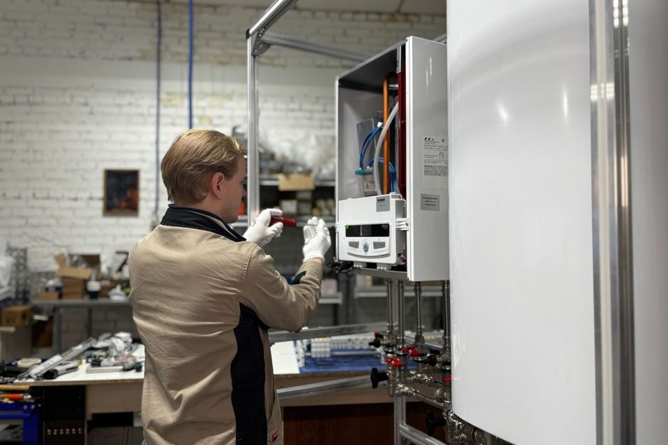 Technician servicing a wall-mounted hot water unit in a utility room. Photo by МОБО Модульные Котельные on Pexels