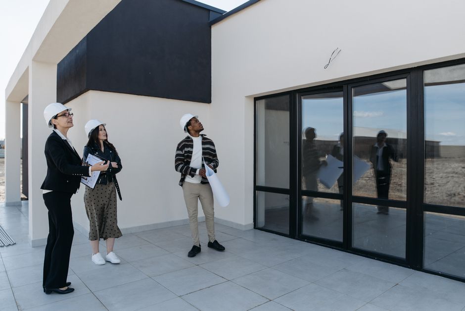 Architects in hard hats discuss the structure of a new building with large glass doors, suggesting a modern architectural design. Photo by Pavel Danilyuk on Pexels