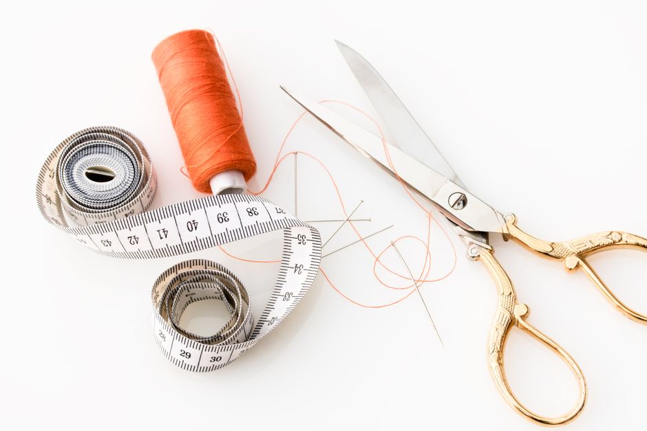 Photo of sewing essentials: scissors, thread, needles, and tape measure on a white background. Photo by Pixabay on Pexels