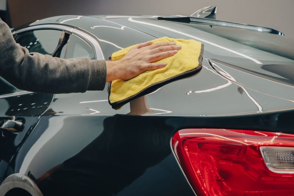 Detailer wiping a car body panel with a yellow microfibre cloth. Photo by Dextar Studio ™ on Pexels