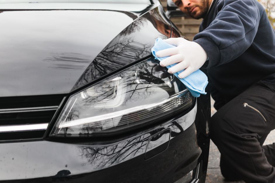 Close-up of a man cleaning a car headlight using a blue cloth outdoors. Photo by El Jundi on Pexels