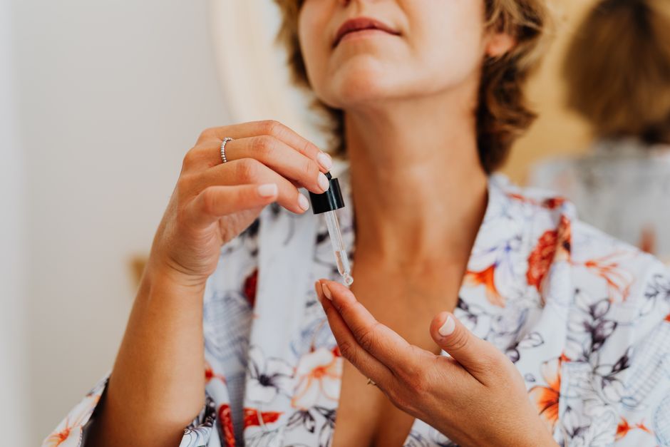 Close-up of a woman in a floral robe applying facial serum using a dropper. Photo by https://kaboompics.com/ on Pexels
