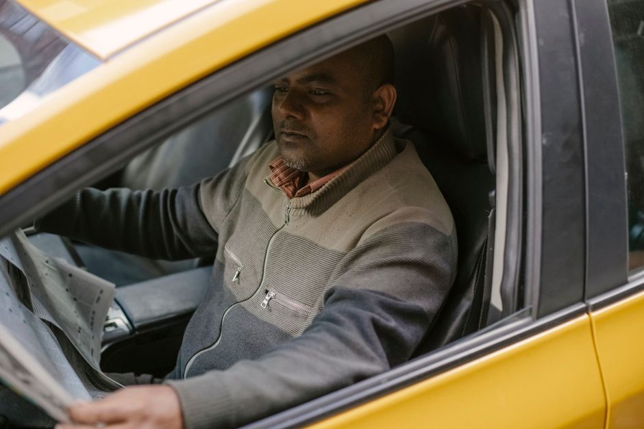 Taxi driver sitting behind the wheel of a yellow cab. Photo by Tim  Samuel on Pexels