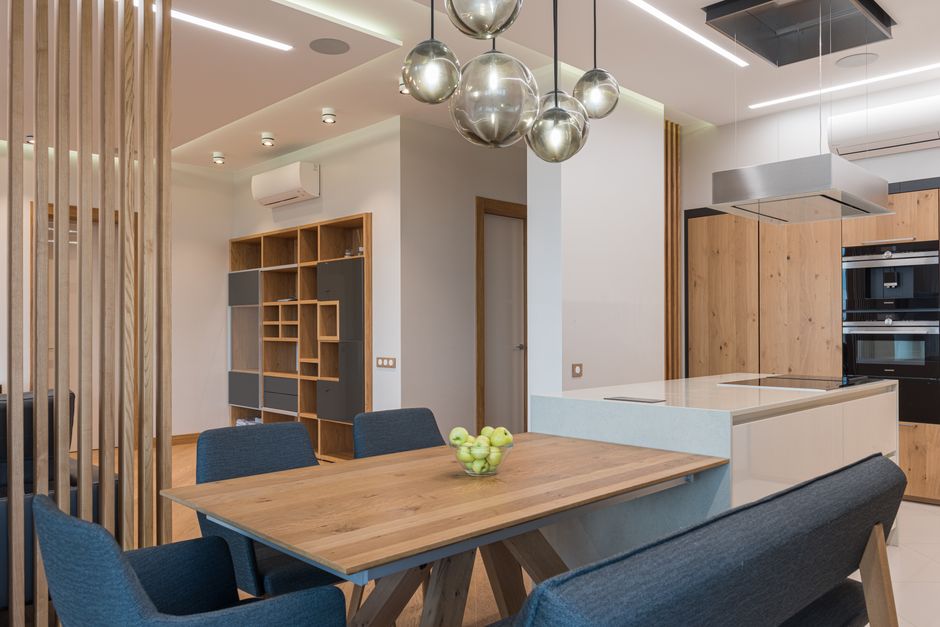 Brown table surrounded with blue chairs in dining room with modern interior and timber shelves. Photo by Max Vakhtbovych on Pexels