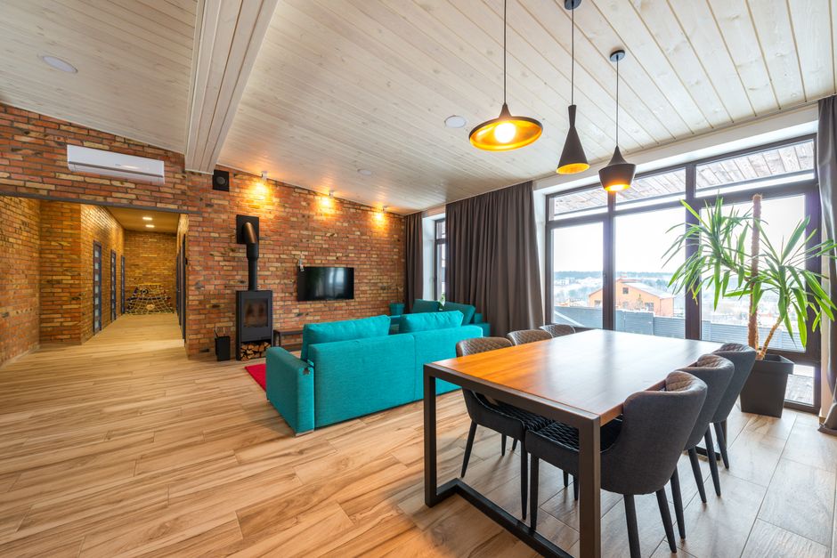 Spacious living room featuring brick walls, teal sofa, and large windows overlooking urban scenery. Photo by Max Vakhtbovych on Pexels