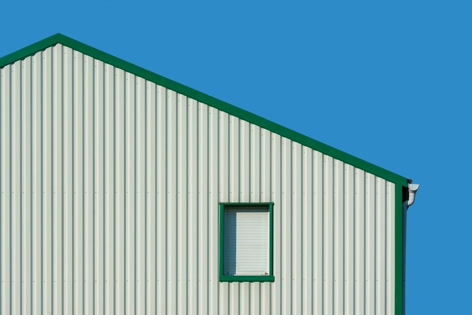 Minimalist building facade against bright blue sky, featuring vertical panels and a single window. Photo by Jan van der Wolf on Pexels