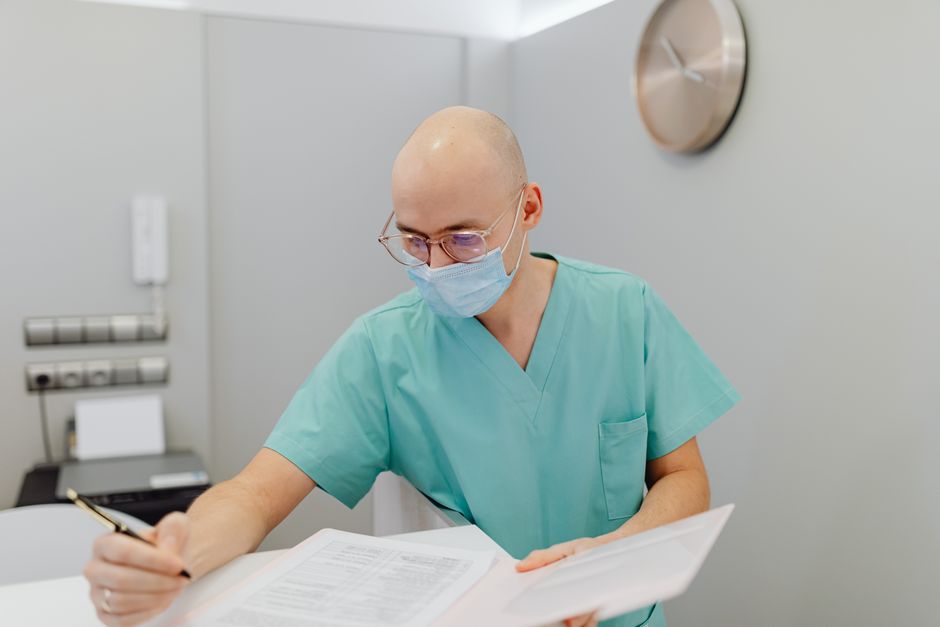 Photo by https://kaboompics.com/ on Pexels Male healthcare worker in scrubs and face mask writing notes in a medical office. Photo by https://kaboompics.com/ on Pexels