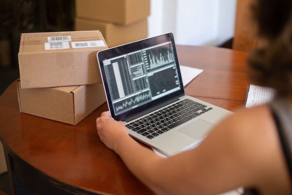 Small business owner checking website analytics on a laptop beside shipping boxes. Photo by Kampus Production on Pexels