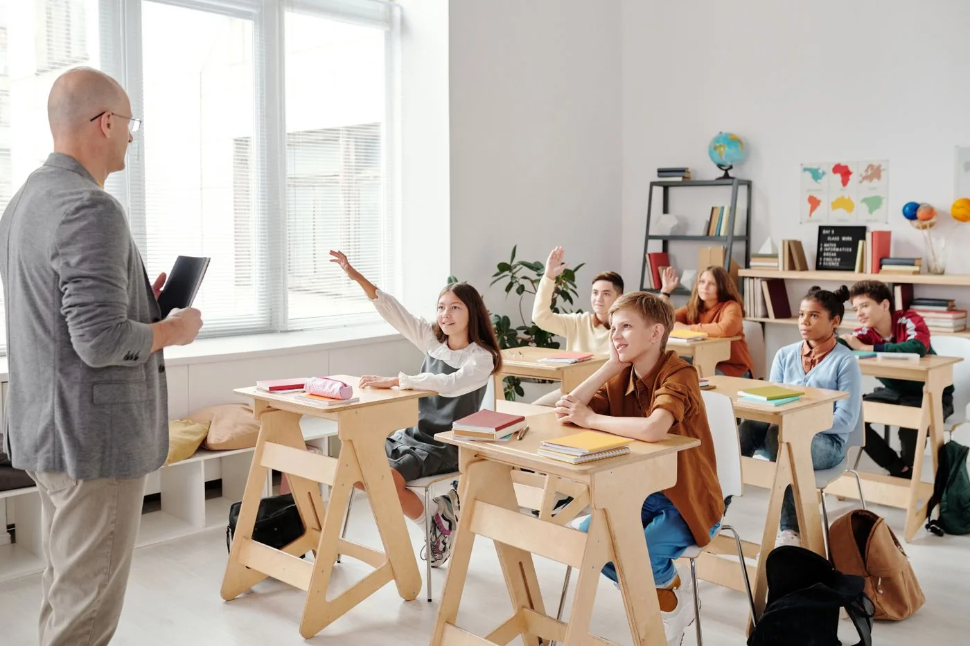Students raising hands in an engaged classroom cohort. Photo by Max Fischer on Pexels