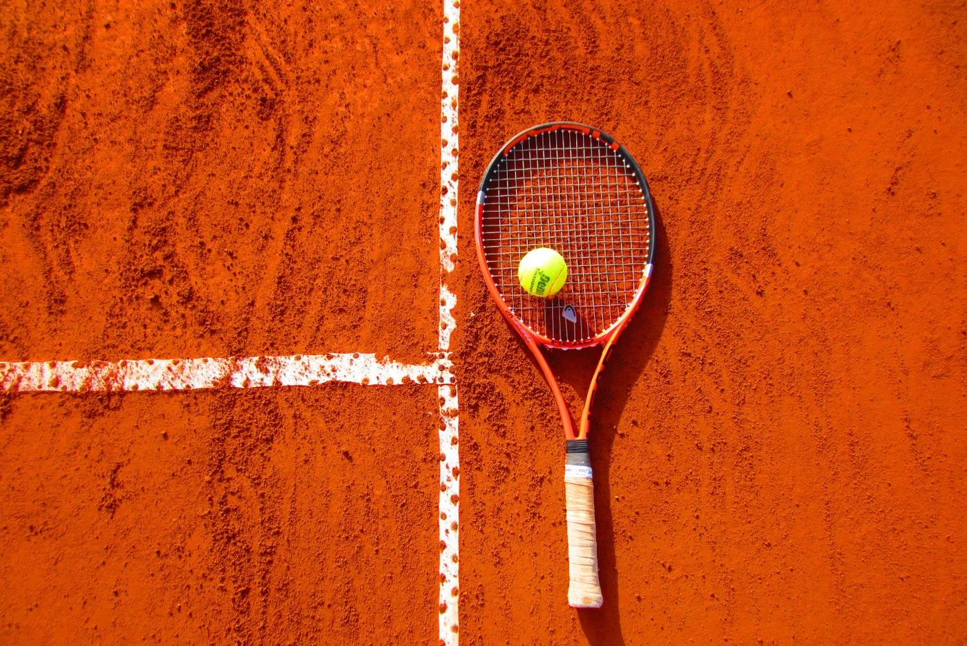 Tennis racket and ball on a clay court for local sports discovery. Photo by Pixabay on Pexels