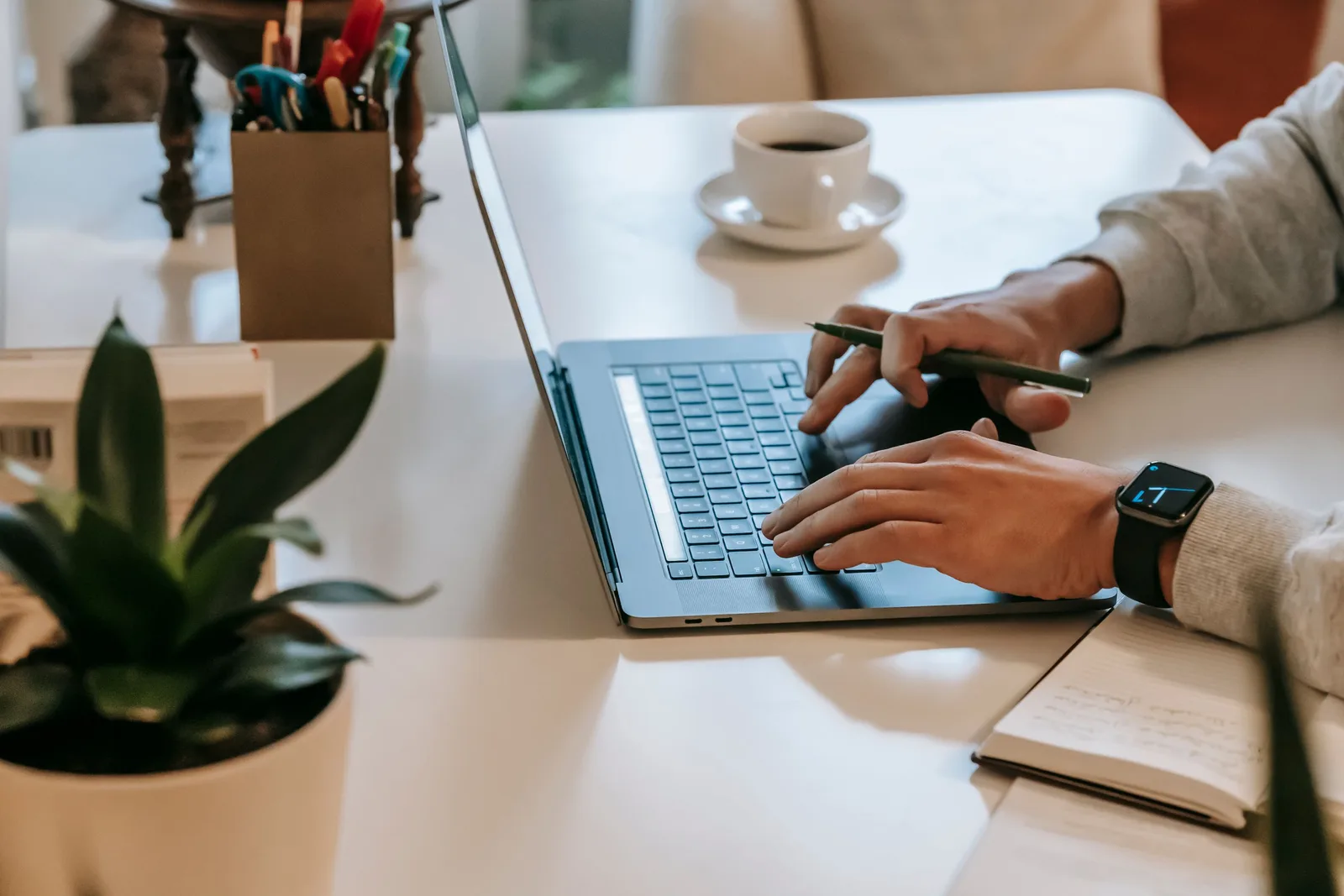 Copywriter typing on a laptop at a white desk with coffee and a plant. Photo by William  Fortunato on Pexels