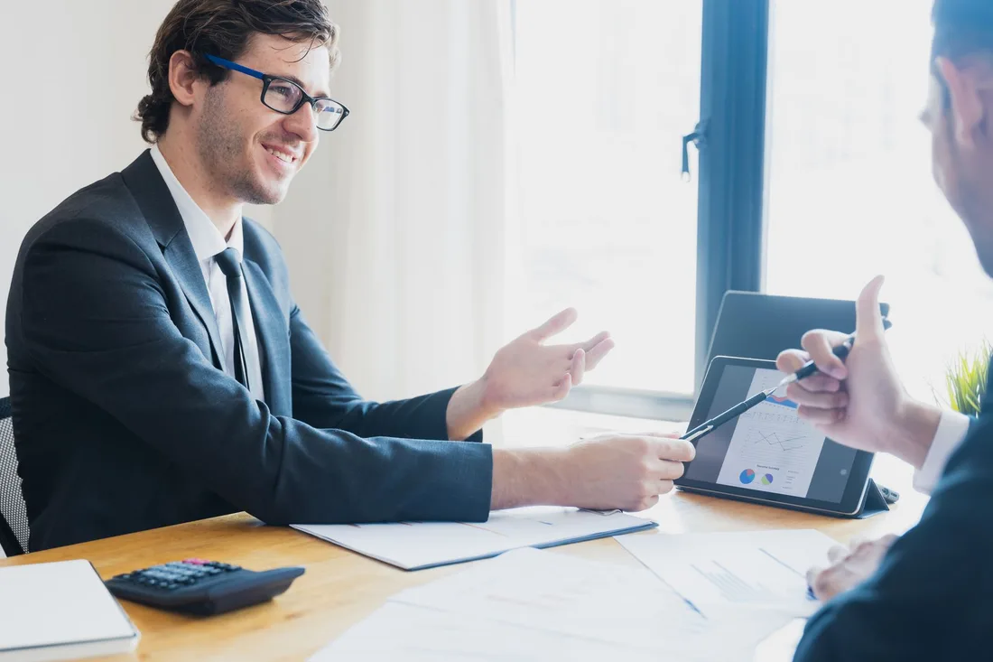 Smiling business owner discussing marketing plans with a consultant at a table with a tablet. Photo by Khwanchai Phanthong on Pexels