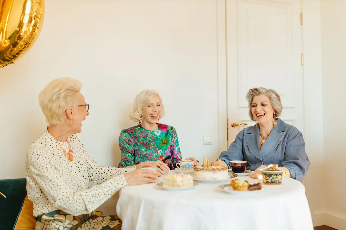 Three elderly women chatting and laughing over tea and cake at a table in the UK. Photo by Yaroslav Shuraev on Pexels