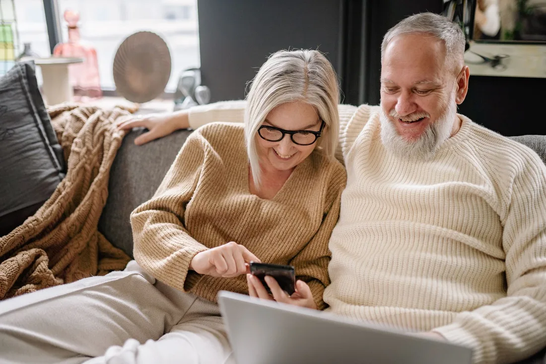Elderly couple smiling together on a sofa looking at a phone in their living room in Singapore. Photo by Yan Krukau on Pexels