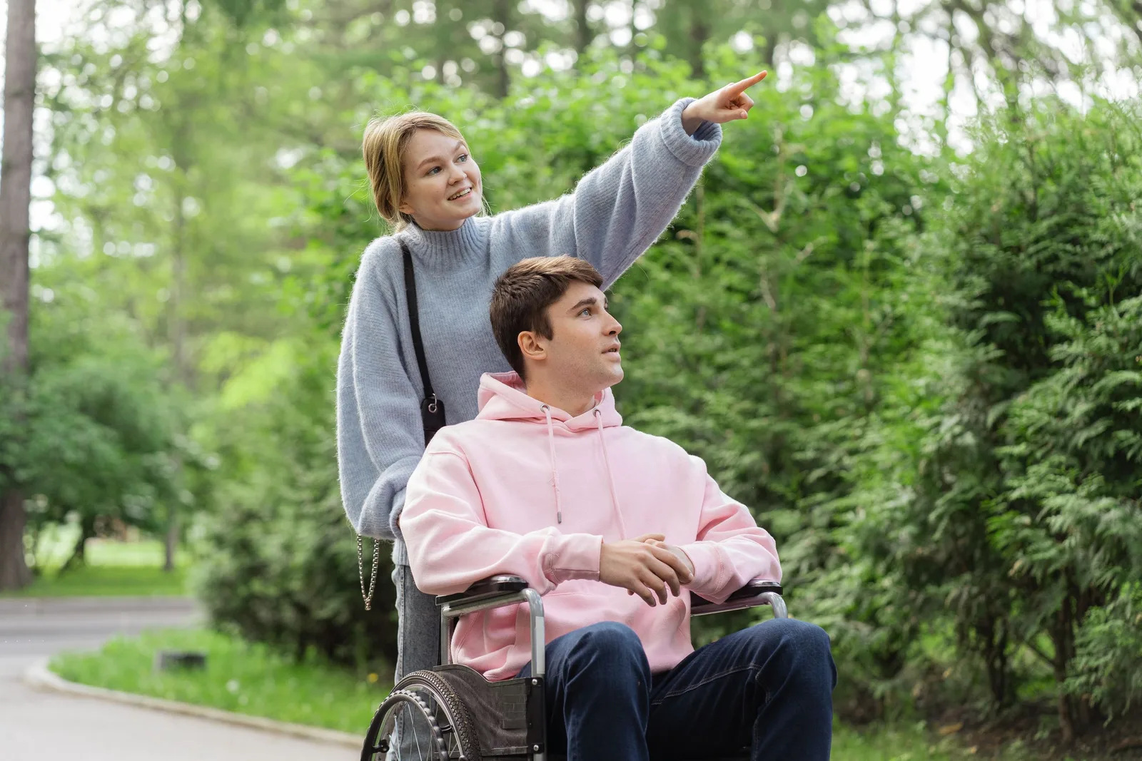 Support worker walking outdoors with a young man in a wheelchair in a green park in Australia. Photo by SHVETS production on Pexels