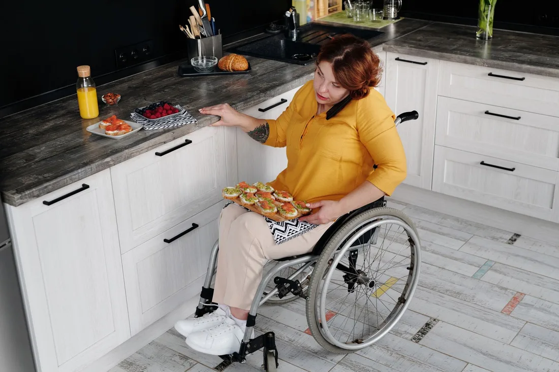 Smiling woman in a wheelchair preparing food independently in a bright kitchen in Australia. Photo by Marcus Aurelius on Pexels