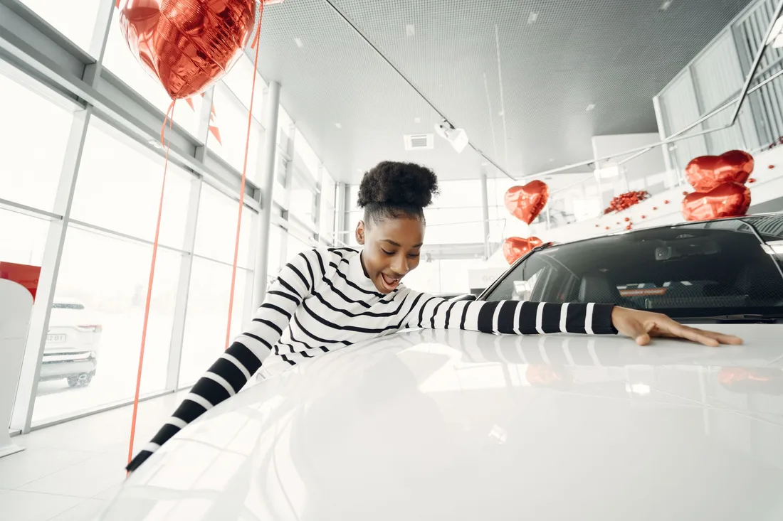 Woman smiling as she runs her hand along a glossy white car in a showroom. Photo by Gustavo Fring on Pexels