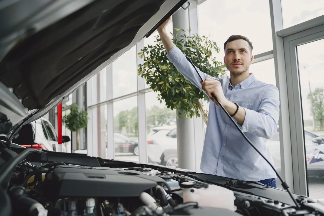 A man carefully checking a car engine in a bright, modern car showroom. Photo by Gustavo Fring on Pexels