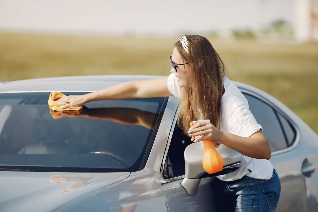 Side view of cheerful female driver in sunglasses and casual clothes cleaning windshield of modern car with microfiber cloth and spray bottle against green field. Photo by Gustavo Fring on Pexels