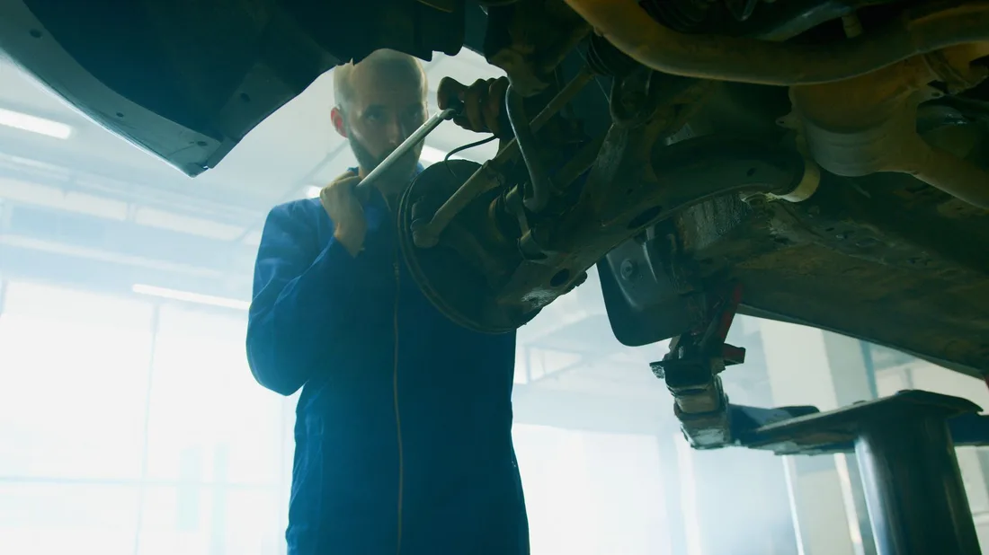 Mechanic in blue coverall fixing a vehicle in a well-lit auto workshop. Photo by Artem Podrez on Pexels