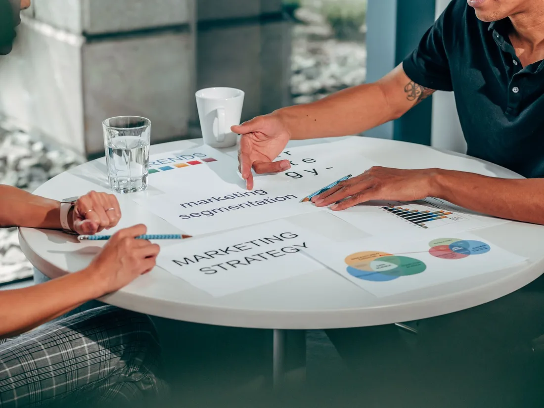 Two adults in an office discussing marketing strategy around a round table. Photo by Kindel Media on Pexels