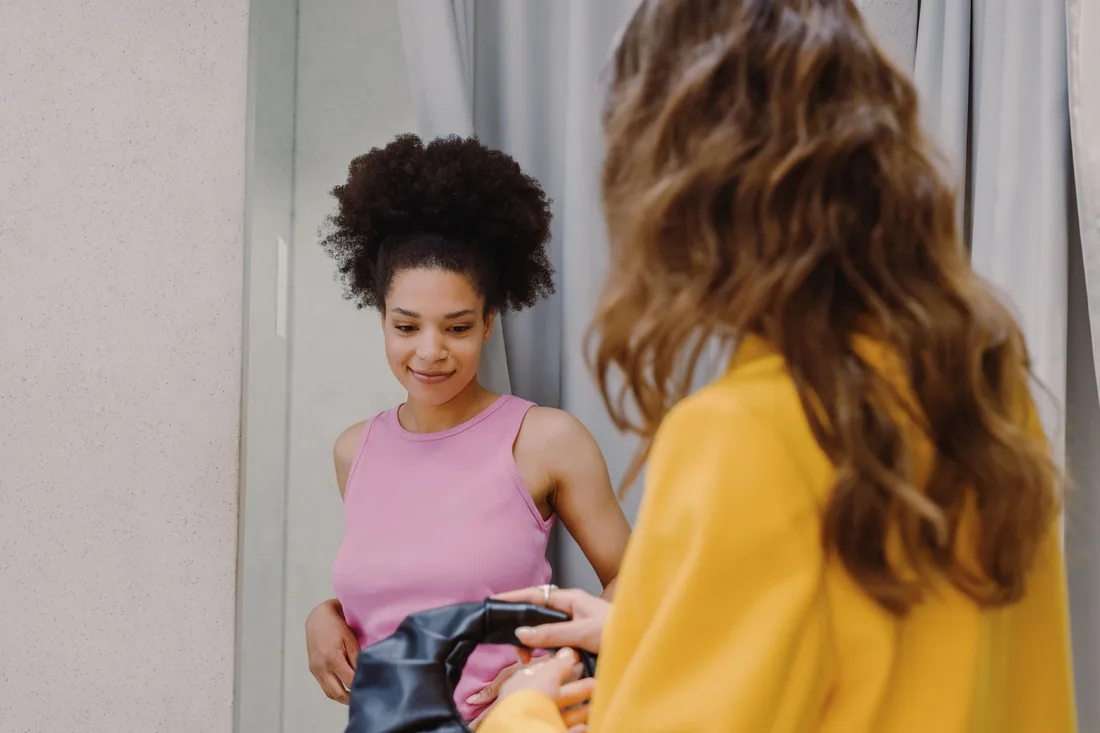 Two women engaged in shopping, trying outfits in a fitting room. Photo by Ron Lach on Pexels