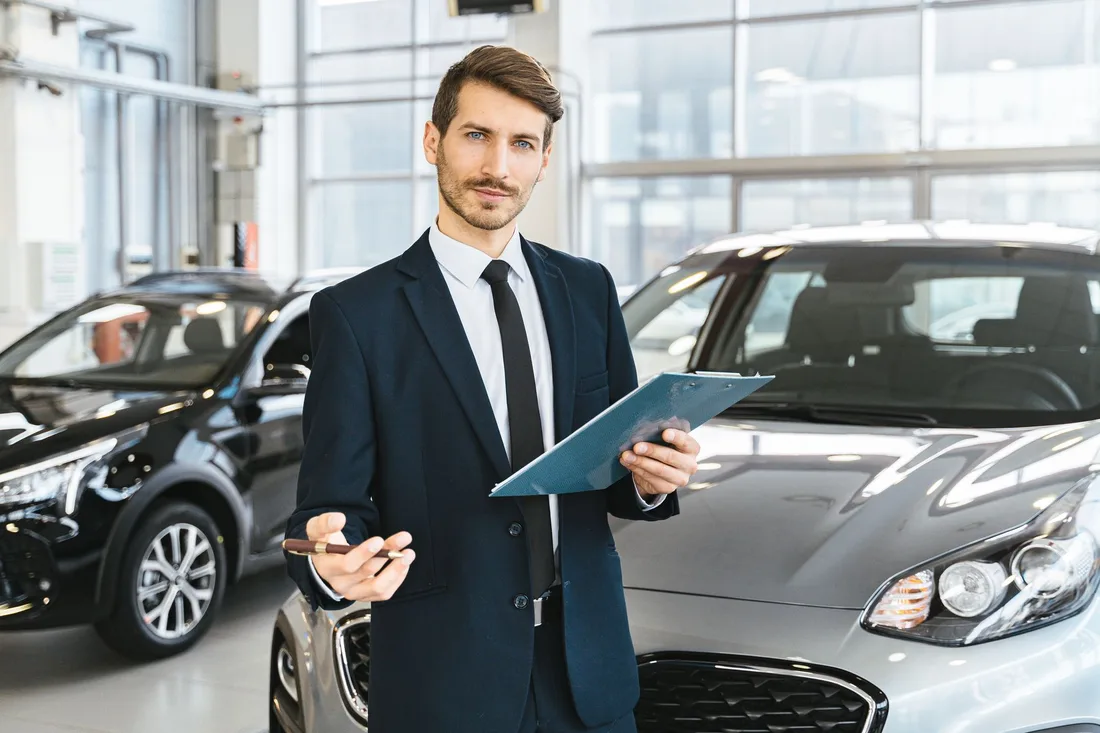 Professional car dealer in business suit holding clipboard in a bright car showroom. Photo by AI25.Studio  Studio on Pexels