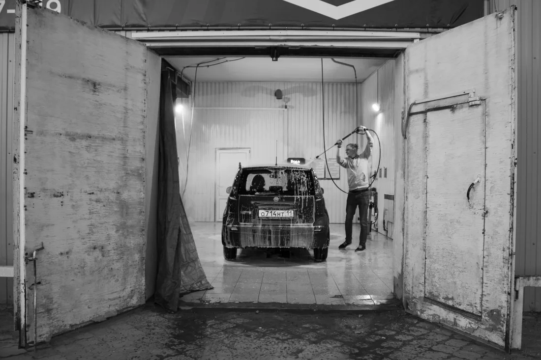 Black and white image of a man washing a car in a garage setting. Photo by Вениамин Курочкин on Pexels